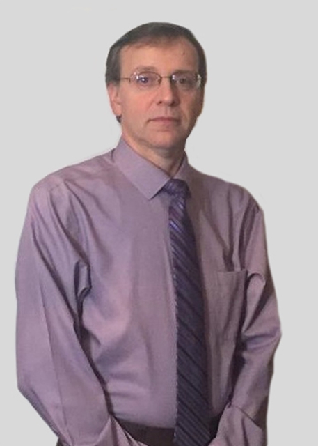 Jim Meyers in professional attire with a purple shirt and patterned tie, standing with his hands clasped.