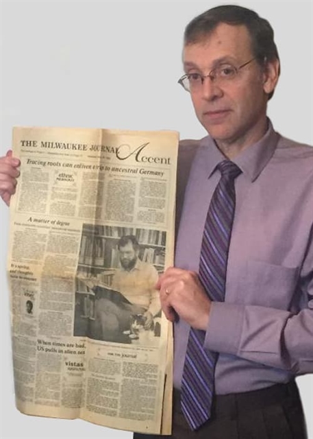 Jim Meyers holding an old newspaper article featuring a black and white photo of a man.