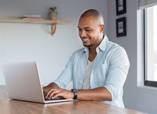 A smiling young man sitting at a table using a laptop computer